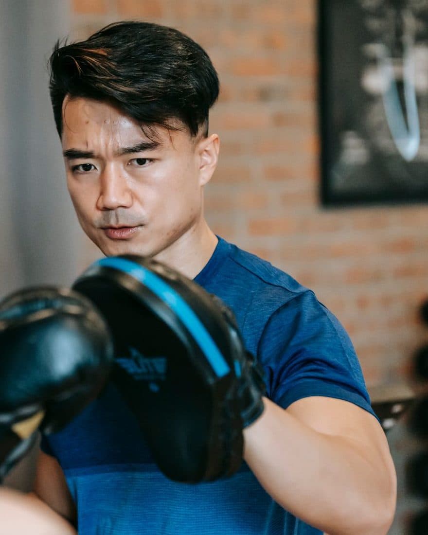 Martial arts coach holding focus mitts for a student during a pad-work session in a boxing gym