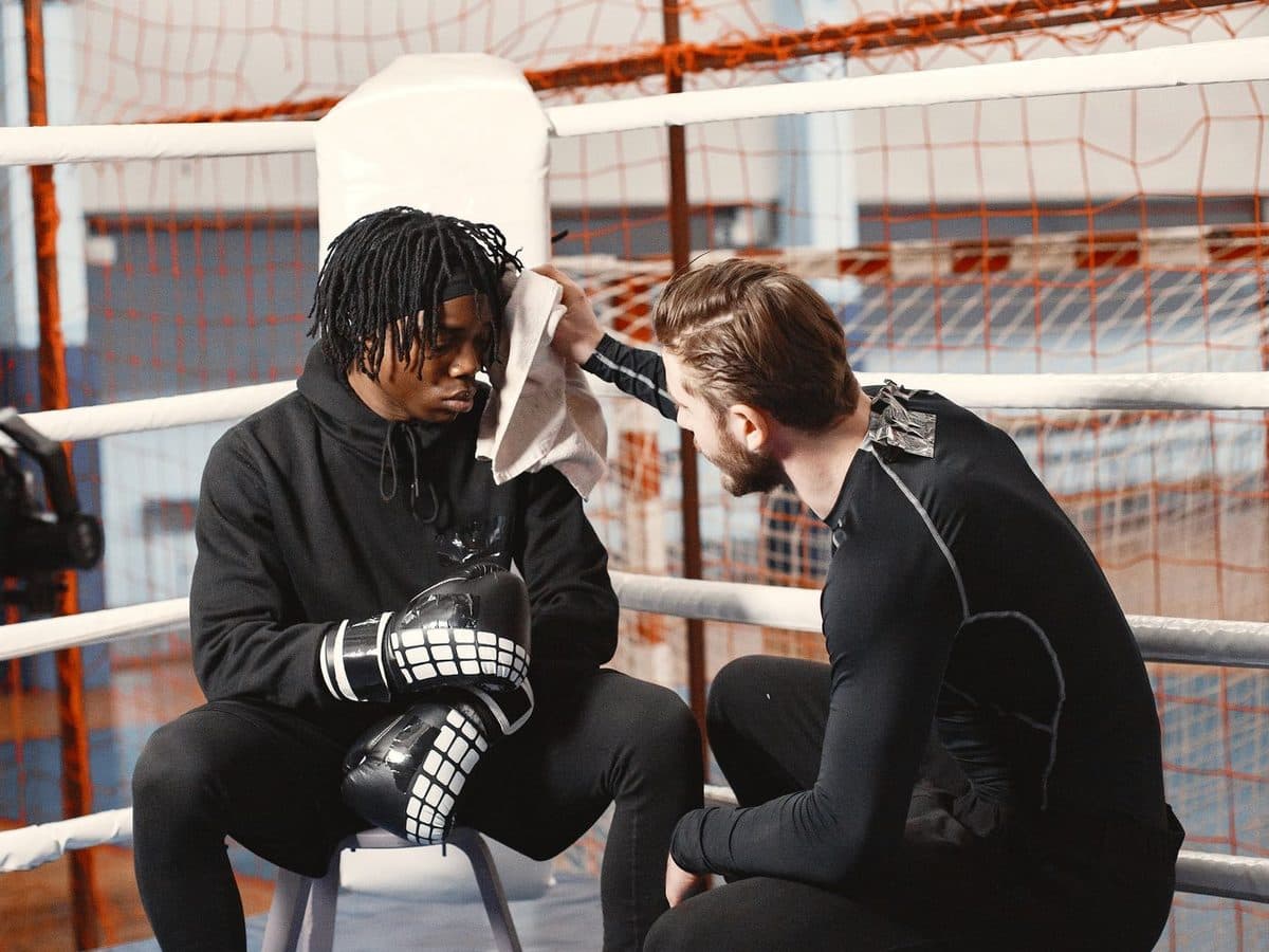 Boxing coach kneeling beside his fighter in the ring, checking in and encouraging him during a martial arts gym training session