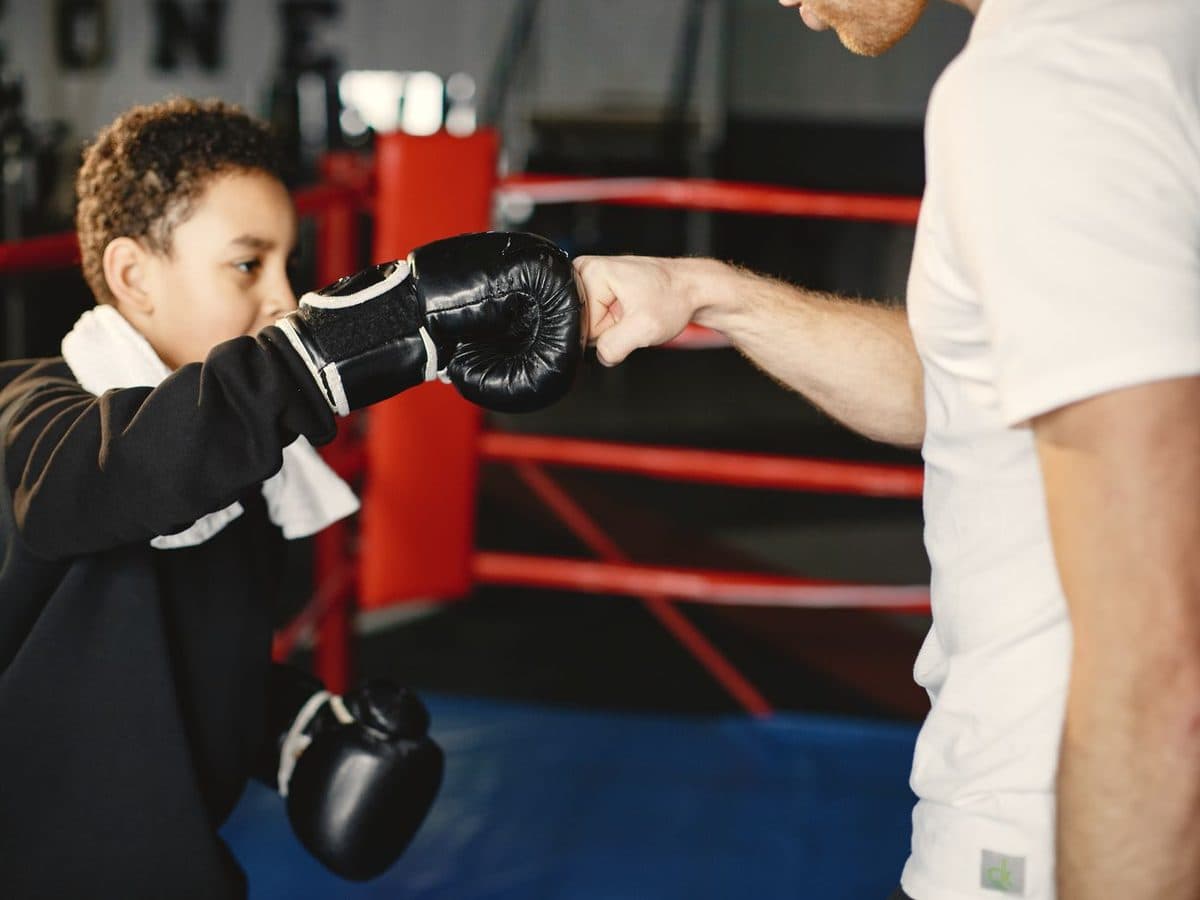 Young boxer in gloves fist-bumping his coach in a red-roped ring at a martial arts gym